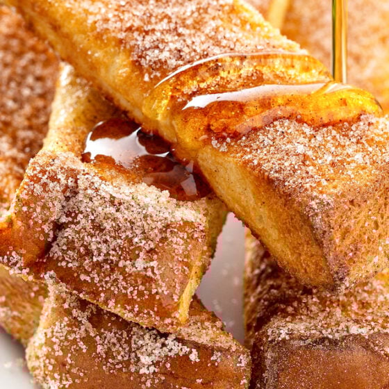 syrup is being poured over a stack of French toast sticks on a white plate.