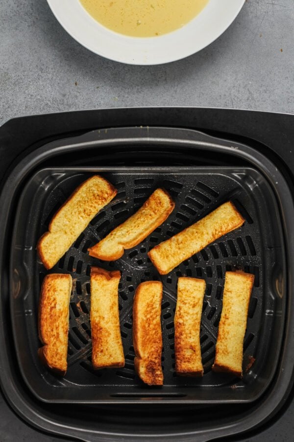 French toast sticks are fully cooked in the basket of an air fryer.