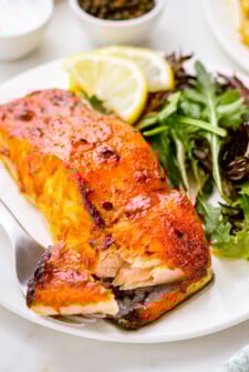 A fork breaking a bite of salmon away from a fillet.