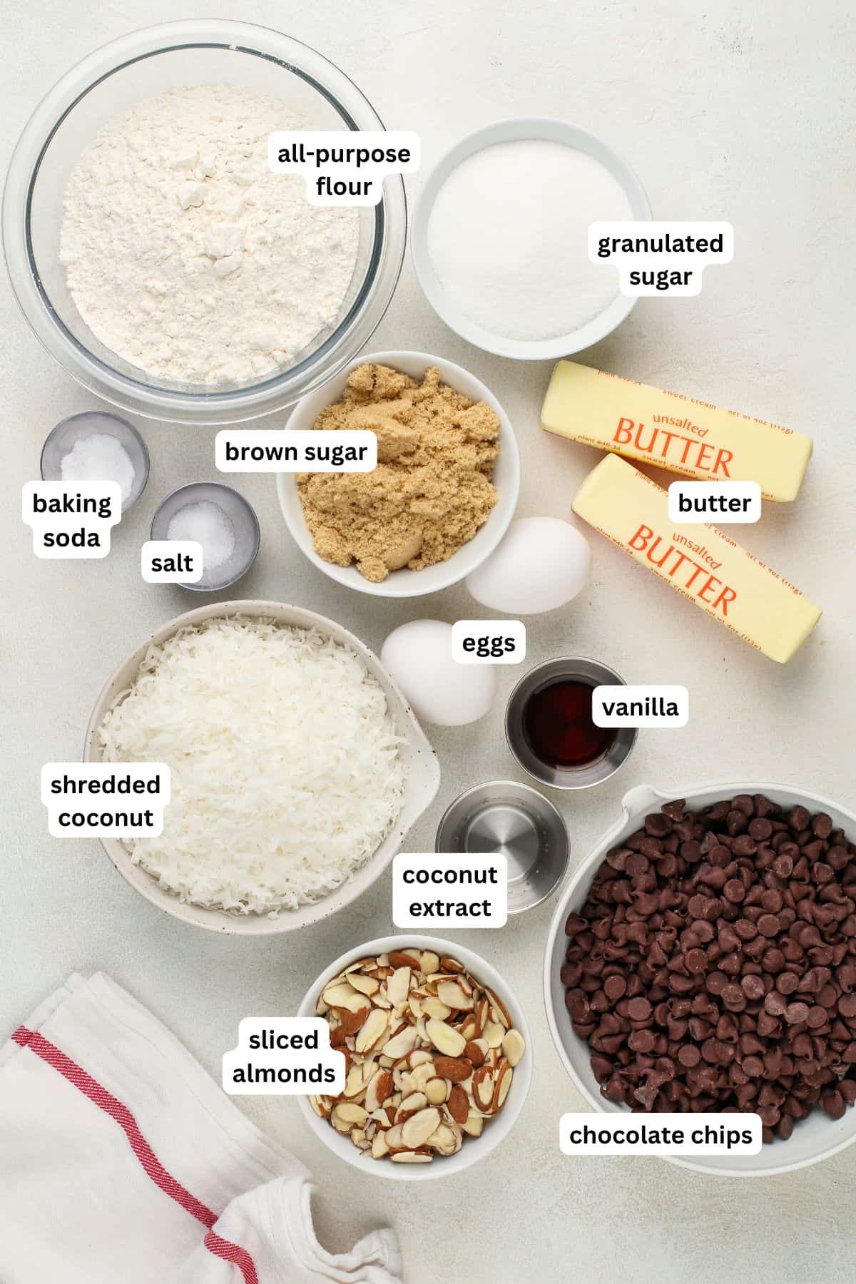 These easy-to-make Almond Joy Cookies are just like the candy bar with a chewy, chocolatey, and nutty bite that's loaded with coconut flavor! Ingredients for almond joy cookie recipe in order from top to bottom: all purpose flour, granulated sugar, baking soda, salt, brown sugar, butter, eggs, shredded coconut, vanilla, coconut extract, sliced almonds, chocolate chips.