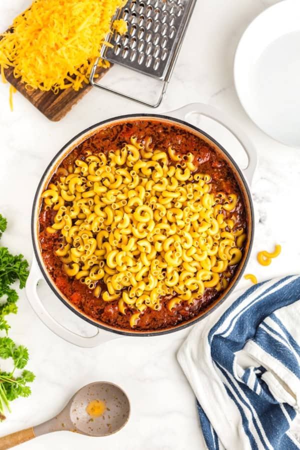 This easy, one-pot Beef Goulash recipe is comfort food at its best with cheesy ground beef and tender noodles in a robust tomato sauce. Uncooked macaroni noodles mixed into a large white pot.