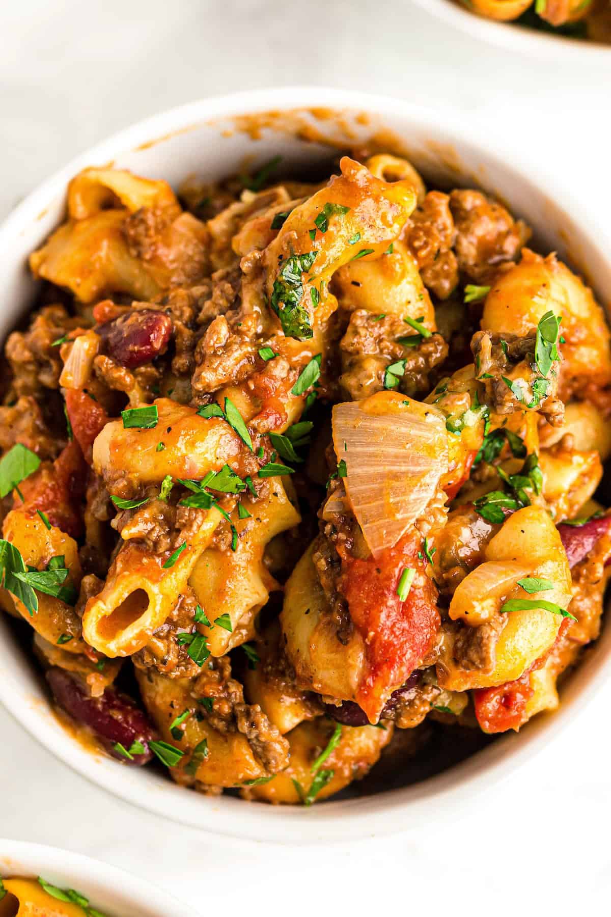 This easy, one-pot Beef Goulash recipe is comfort food at its best with cheesy ground beef and tender noodles in a robust tomato sauce. A single serving of American goulash is served in a white bowl.