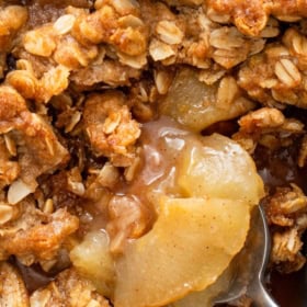 Close-up of old fashioned apple crisp recipe with a golden oat topping and soft baked apple slices, a spoon scooping out a portion.