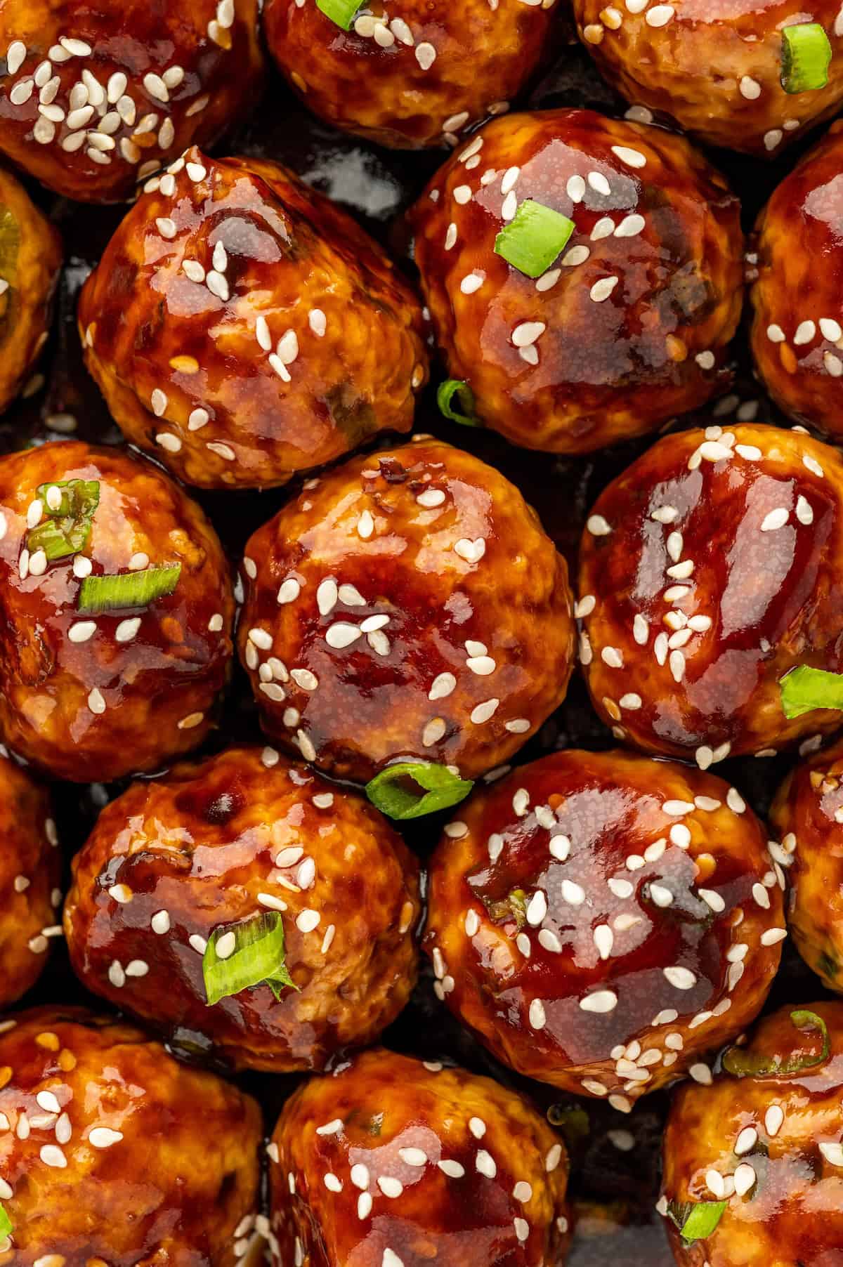 These sweet and savory Asian Chicken Meatballs are infused with fresh ginger and garlic, then baked and coated in a sticky honey-soy glaze. Chopped green onions and sesame seeds garnish a large portion of asian meatballs.