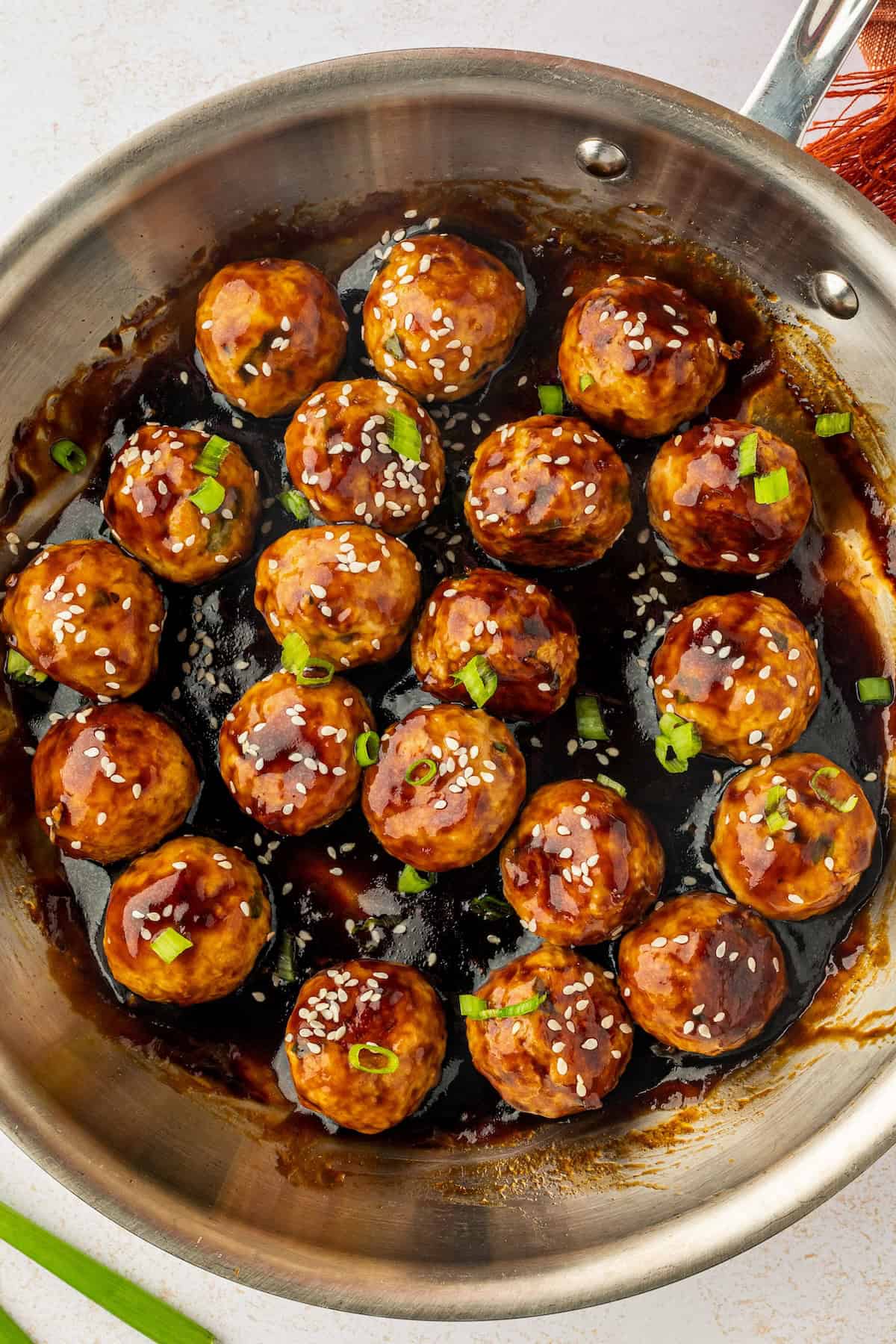 These sweet and savory Asian Chicken Meatballs are infused with fresh ginger and garlic, then baked and coated in a sticky honey-soy glaze. A pan of asian chicken meatballs coated in thick, glossy sauce.