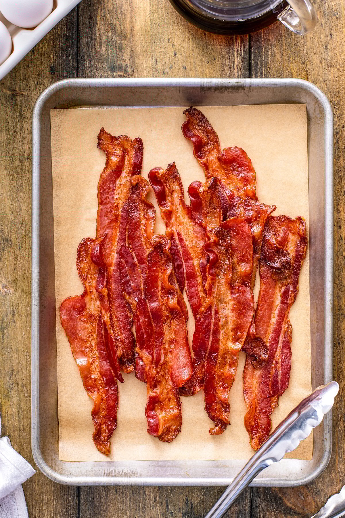 Whether you like it extra crispy or slightly tender, here are two mess-free ways for how to cook bacon in the oven to perfection, every time! Crispy cooked bacon in oven after draining on paper towels. Bacon is arranged on top of a parchment paper lined baking sheet with tongs.