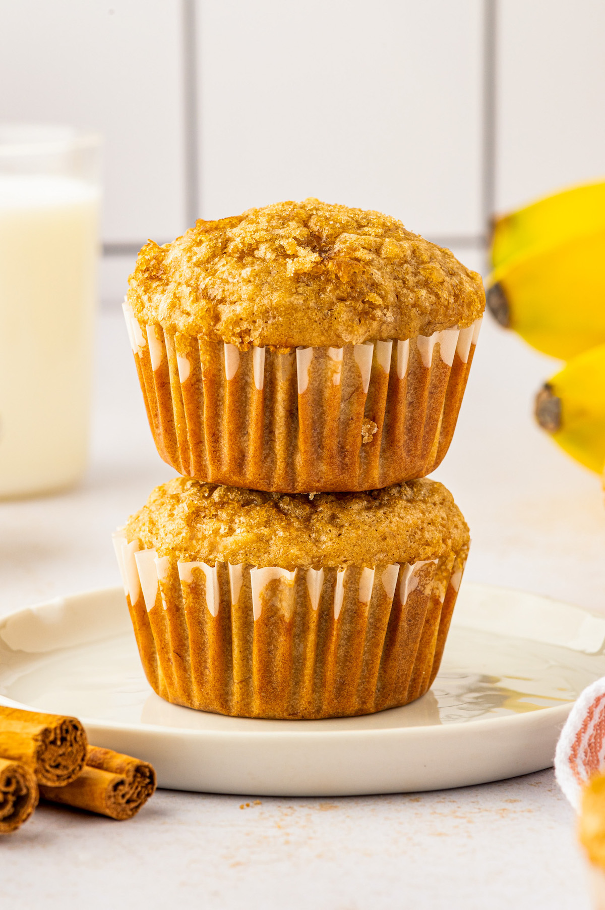 Made in one-bowl in just 25 minutes, these easy Brown Sugar Banana Muffins are extra moist with a caramelized brown sugar crunchy topping! Two stacked brown sugar banana muffins on a plate.