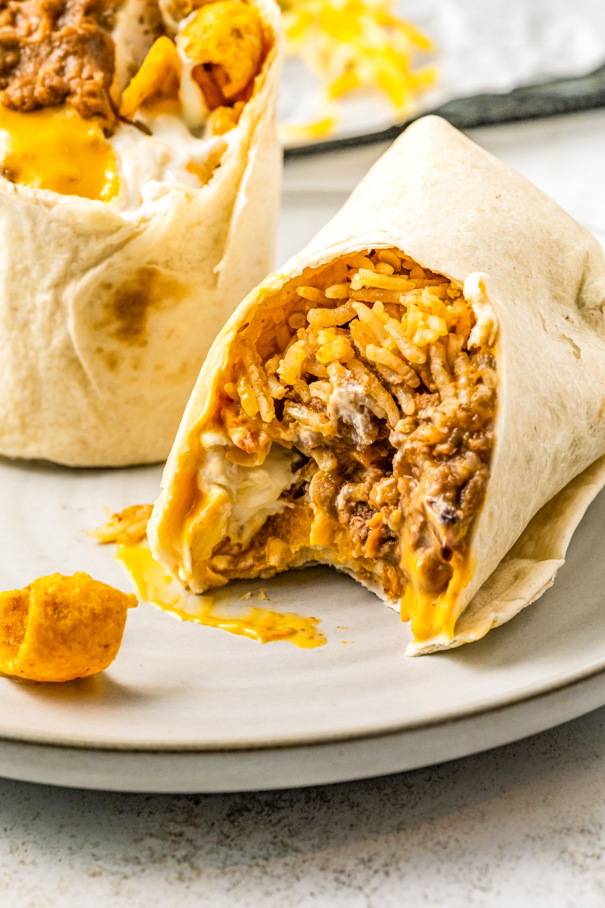 A copycat of the fast-food favorite, this Taco Bell Beefy Melt Burrito is stuffed with seasoned beef, refried beans, rice, Fritos, and more! A burrito cut in half and placed on a dinner plate. One of the burritos has had a bite taken out of it.