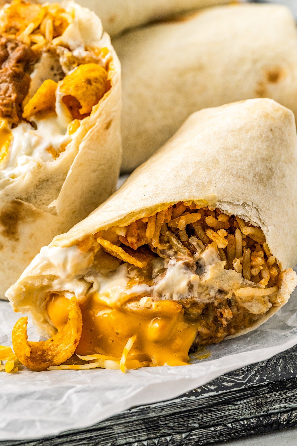 A copycat of the fast-food favorite, this Taco Bell Beefy Melt Burrito is stuffed with seasoned beef, refried beans, rice, Fritos, and more! Close-up of half a burrito, cut on the diagonal with cheese and chips spilling out.