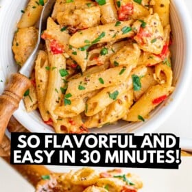 A serving spoon scooping a spoonful of creamy cajun chicken pasta out of a skillet and served in a bowl with fresh herbs on top.