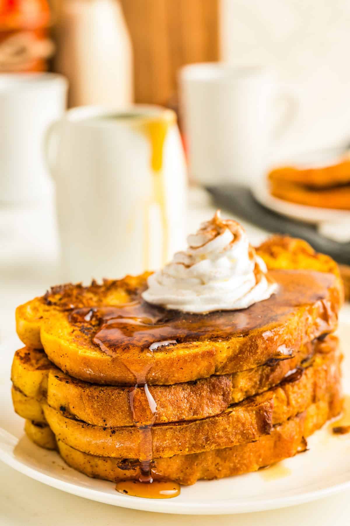 Packed with pumpkin pie flavor, this quick and easy pumpkin French toast, served with maple syrup or powdered sugar, will disappear quickly! Syrup is poured generously all over a stack of pumpkin French toast on a white plate.