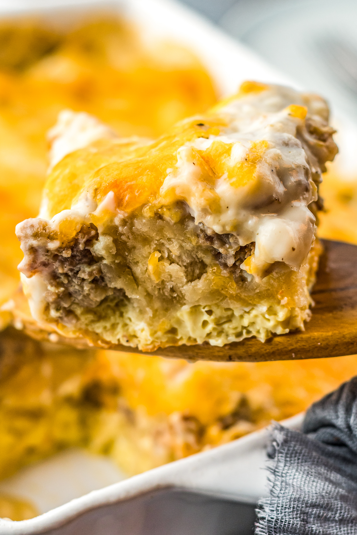 This easy Sausage Biscuits and Gravy Casserole recipe is filled with hearty layers of flaky biscuits, cheesy eggs, and creamy sausage gravy! A serving of biscuits and gravy breakfast casserole is lifted from a baking dish.