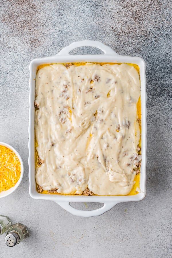 This easy Sausage Biscuits and Gravy Casserole recipe is filled with hearty layers of flaky biscuits, cheesy eggs, and creamy sausage gravy! White gravy spread over cooked sausage.