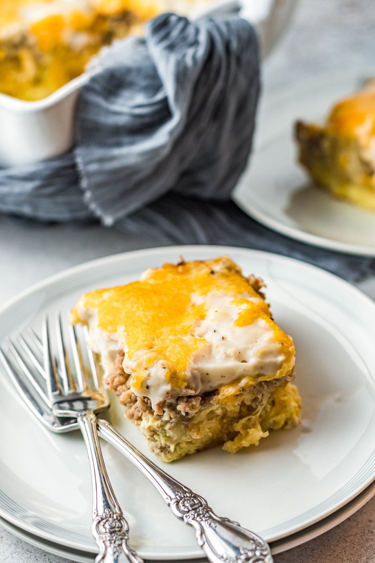 This easy Sausage Biscuits and Gravy Casserole recipe is filled with hearty layers of flaky biscuits, cheesy eggs, and creamy sausage gravy! A single serving of sausage gravy biscuit casserole on a white plate with two forks.