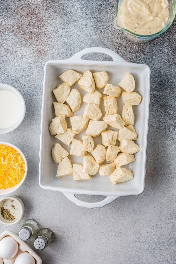 This easy Sausage Biscuits and Gravy Casserole recipe is filled with hearty layers of flaky biscuits, cheesy eggs, and creamy sausage gravy! Biscuit pieces in the bottom of a baking dish.