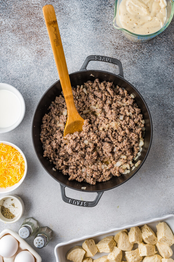 This easy Sausage Biscuits and Gravy Casserole recipe is filled with hearty layers of flaky biscuits, cheesy eggs, and creamy sausage gravy! Cooked sausage and onion in a skillet.