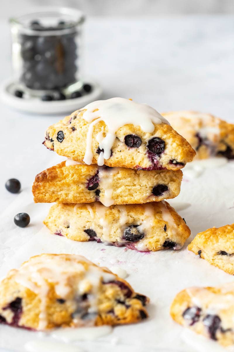 These Blueberry Scones are soft, flaky and bursting with blueberries. Add a creamy vanilla glaze and this easy scone recipe is a real treat! A stack of three blueberry scones drizzled with vanilla glaze.