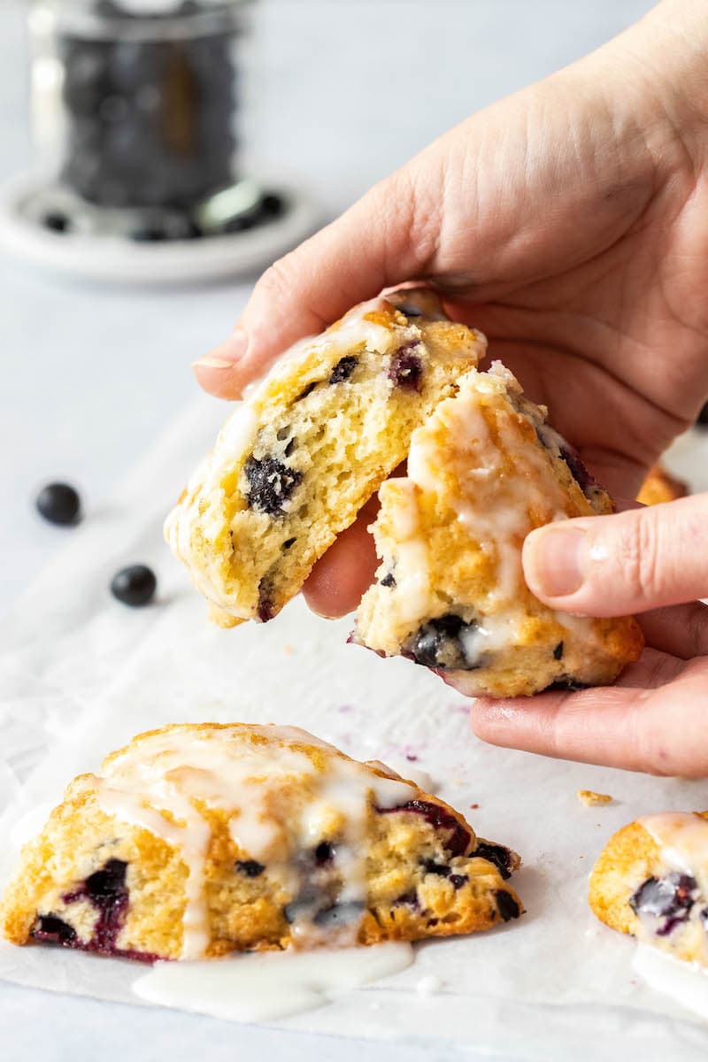 These Blueberry Scones are soft, flaky and bursting with blueberries. Add a creamy vanilla glaze and this easy scone recipe is a real treat! A glazed blueberry scone broken in half.