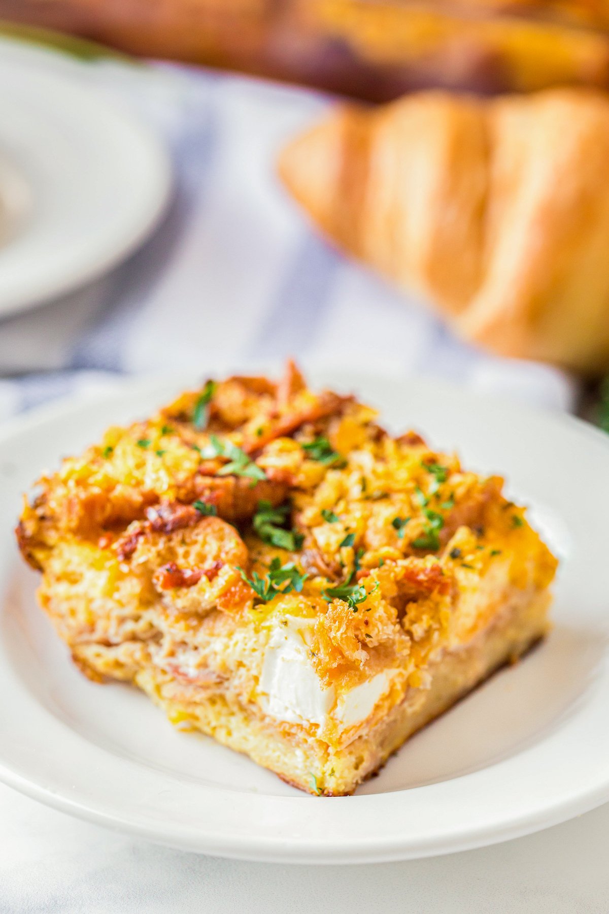 This overnight breakfast casserole with ham is made with flaky croissants, cream cheese and a crispy, buttery cornflake topping for crunch! A slice of Breakfast Casserole With Ham and cream cheese on a plate.