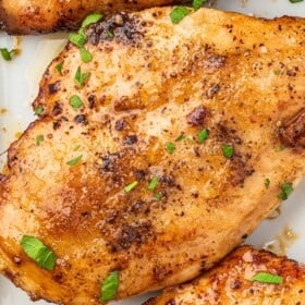 Three garlic brown sugar chicken breasts on a platter topped with fresh herbs.