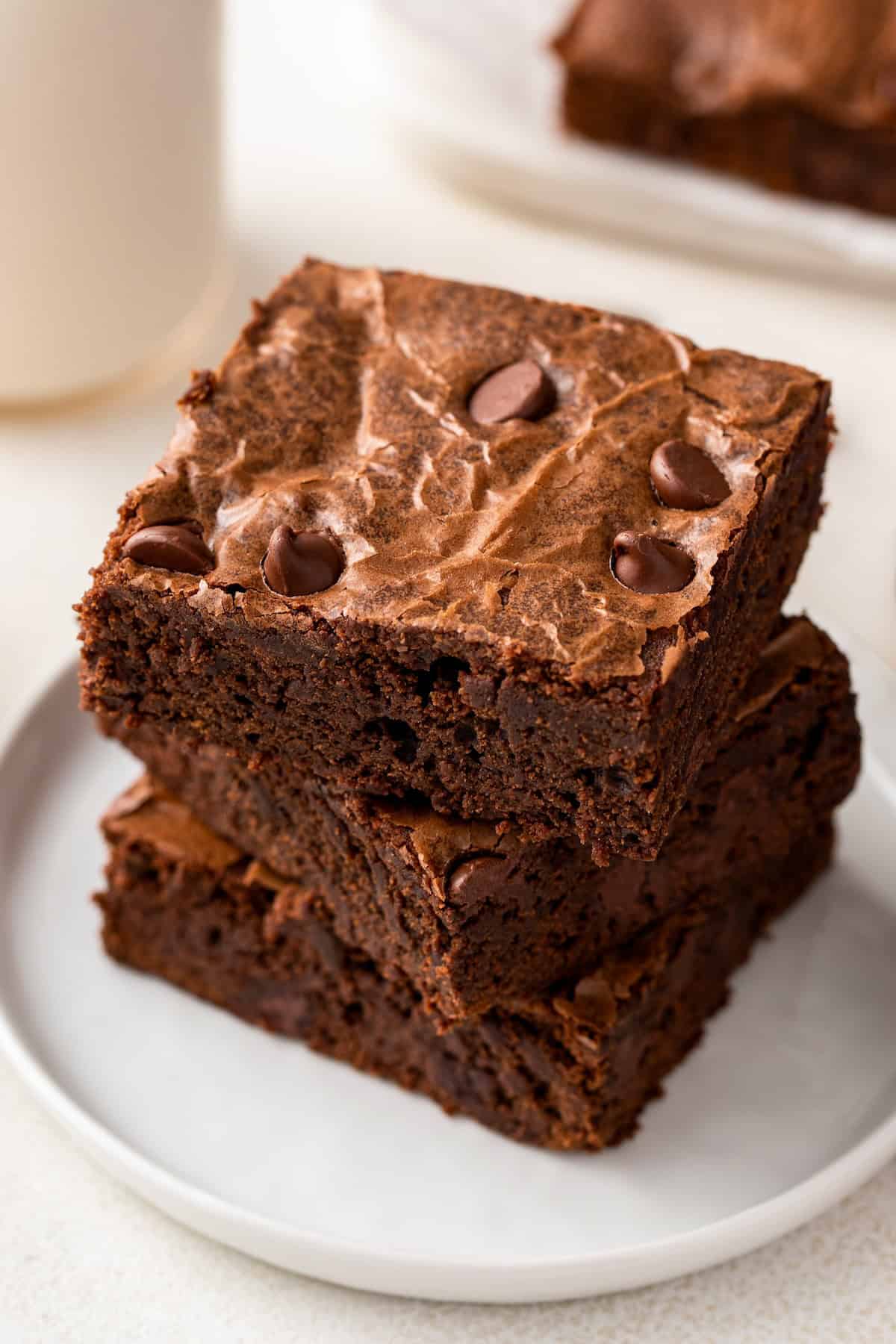 Made easy in just one-bowl, this fudge-y Homemade Brownie recipe delivers the perfect rich and chewy brownie with a crackly top! A stack of rich brownies from scratch are placed on a white plate.