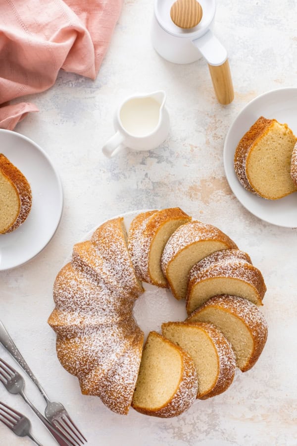 This easy homemade buttermilk pound cake recipe is perfectly dense, moist, and buttery with just the right touch of tang and sweetness. Sliced cake on a platter with powdered sugar dusted on top and two small plates with slices of cake on them for serving.