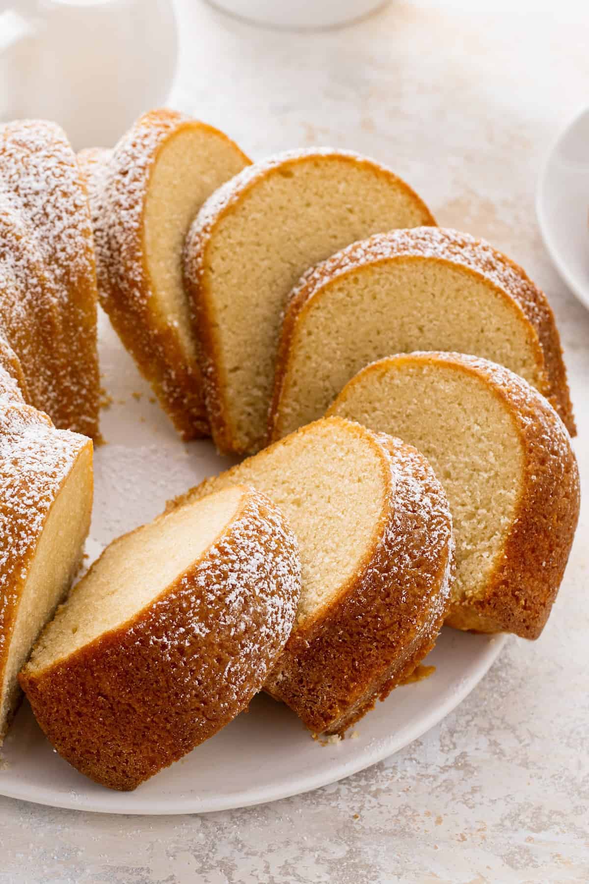 This easy homemade buttermilk pound cake recipe is perfectly dense, moist, and buttery with just the right touch of tang and sweetness. Buttermilk pound cake sliced into pieces dusted with powdered sugar on top.