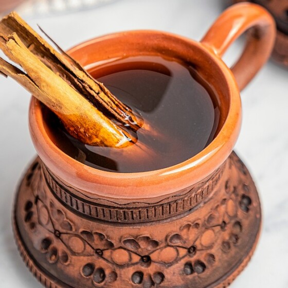 A clay mug filled with Café de Olla with a cinnamon stick.