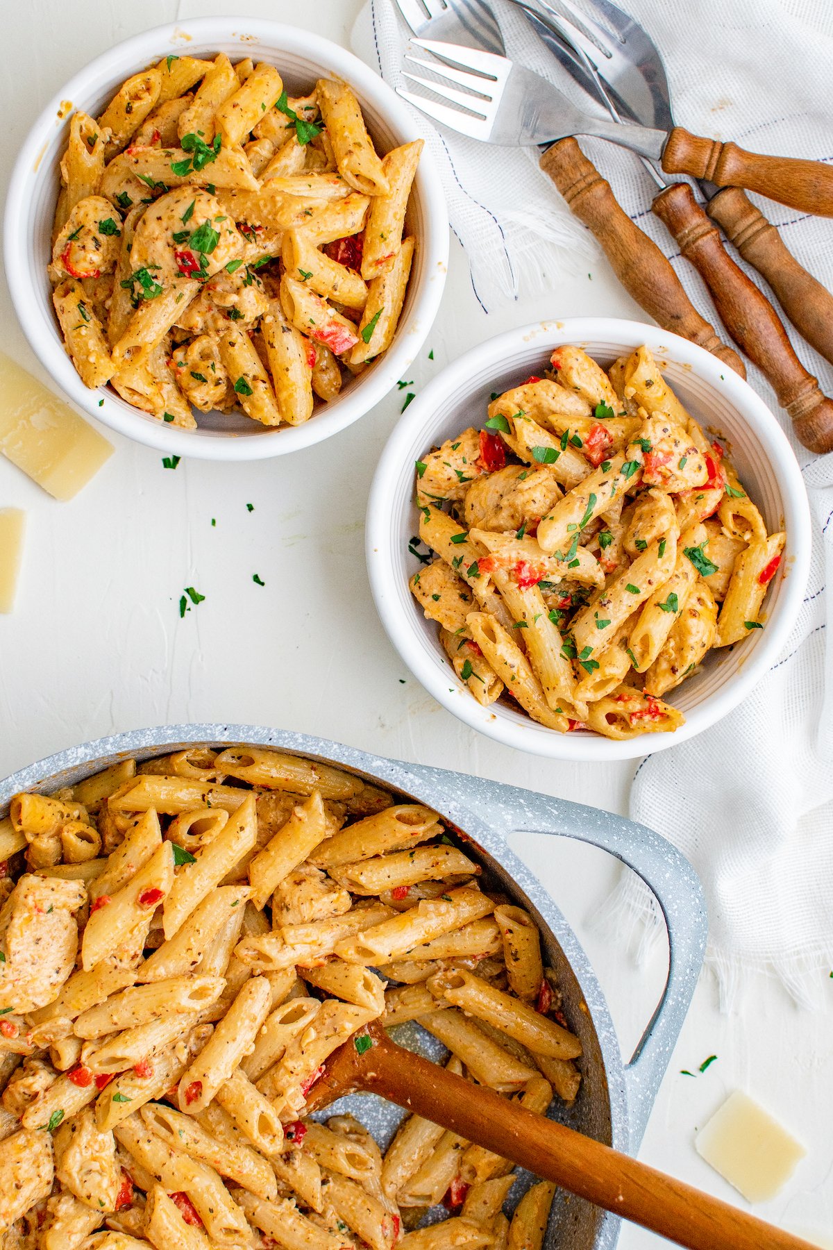 This flavorful and creamy Cajun Chicken Pasta recipe is one of our favorite restaurant style dishes to make at home in just 30 minutes! Two bowls of Cajun chicken pasta with a pot of cajun pasta with a wooden serving spoon.