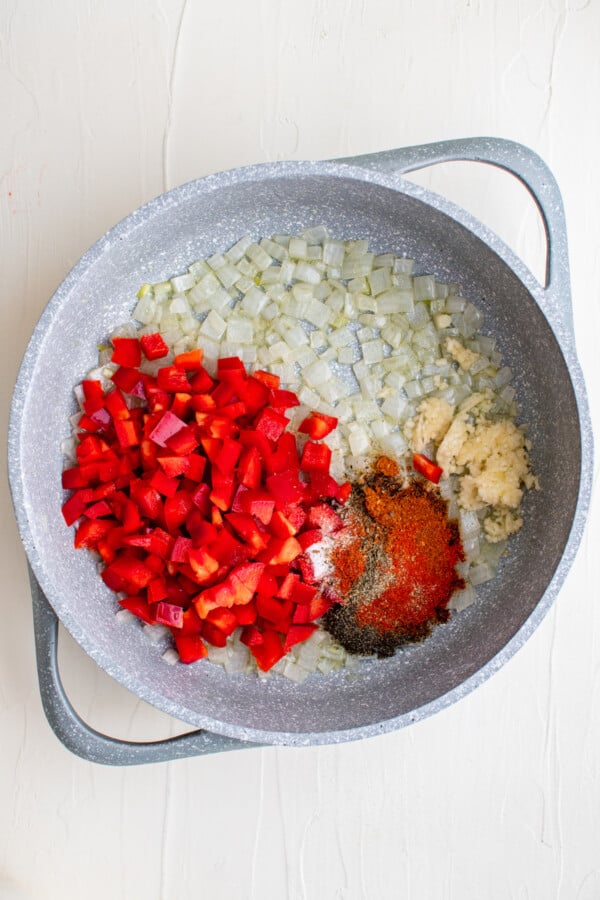 This flavorful and creamy Cajun Chicken Pasta recipe is one of our favorite restaurant style dishes to make at home in just 30 minutes! Red bell pepper with onion, garlic and seasonings in a pan.