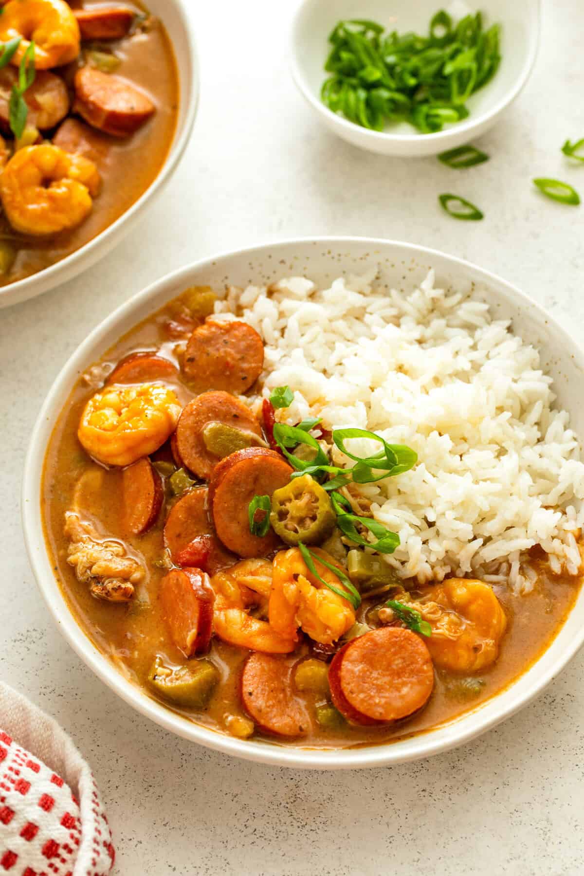 Passed down through generations, this authentic Cajun Gumbo recipe is made with a smoky, flavorful dark roux and your choice of proteins. White rice and seafood gumbo served in a single white bowl.