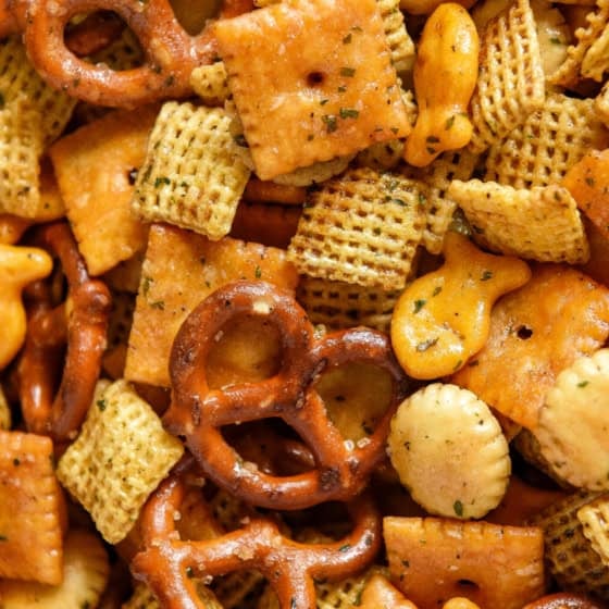A close-up of a homemade chex mix featuring pretzels, cheese crackers, oyster crackers, goldfish crackers, and square cereal pieces, all coated with seasoning.