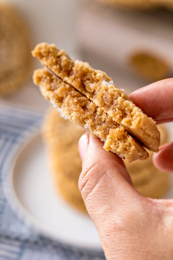 The BEST chewy peanut butter cookies with soft chewy centers, crispy edges and tons of peanut butter flavor! Easy recipe ready in 30 minutes! A chewy peanut butter cookie broken in half to show the inside and being held by two fingers.