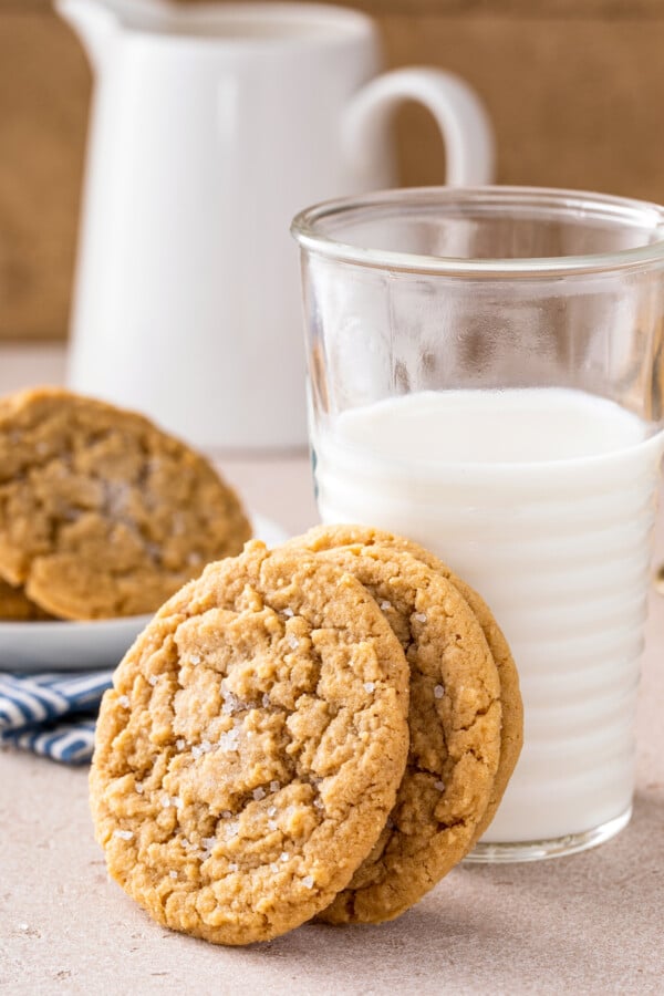 The BEST chewy peanut butter cookies with soft chewy centers, crispy edges and tons of peanut butter flavor! Easy recipe ready in 30 minutes! Three chewy peanut butter cookies stacked against a glass of cold milk.