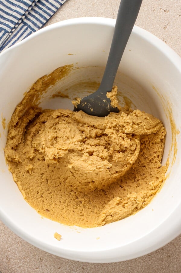 The BEST chewy peanut butter cookies with soft chewy centers, crispy edges and tons of peanut butter flavor! Easy recipe ready in 30 minutes! Cookie dough in a mixing bowl with a spatula inserted into the dough.