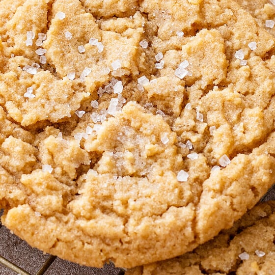 Chewy peanut butter cookies with crisp edges and soft centers stacked on top of each other on a cooling rack.