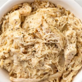 A bowl filled with shredded chicken and gravy, sprinkled with black pepper and herbs.