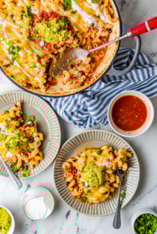 A chicken enchilada pasta bake in a round baking dish, with two servings on dinner plates nearby, along with a dish of salsa.