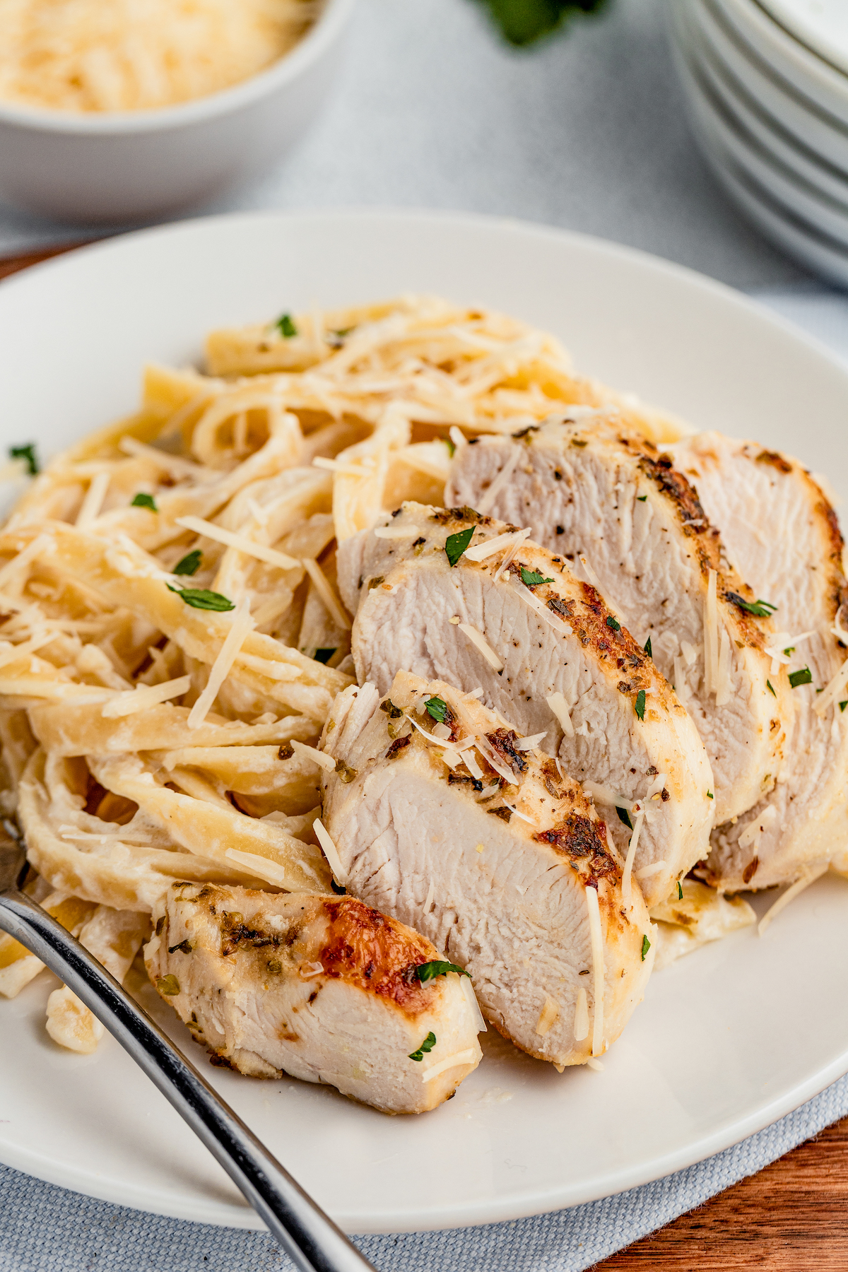 Chicken Alfredo is an easy weeknight dinner that’s worthy of a special occasion, with juicy chicken and a garlicky Parmesan cream sauce. Fettuccine on a plate, with sliced chicken fanned along the side of the pasta.