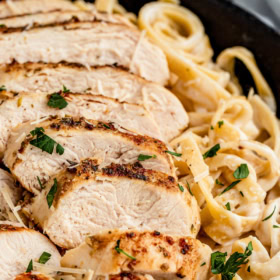 Sliced chicken breast on top of fettuccine in alfredo sauce.