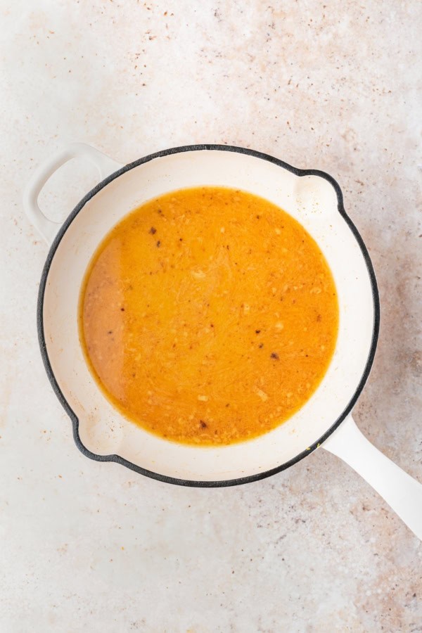 Ready in just 30 minutes, juicy Chicken Piccata Meatballs are simmered in a luscious lemon-caper sauce. Perfect served over pasta or rice! A white pot with a handle contains a yellow-orange lemon sauce with visible small bits of leftover cooked meatball pieces, set on a light-colored textured surface.