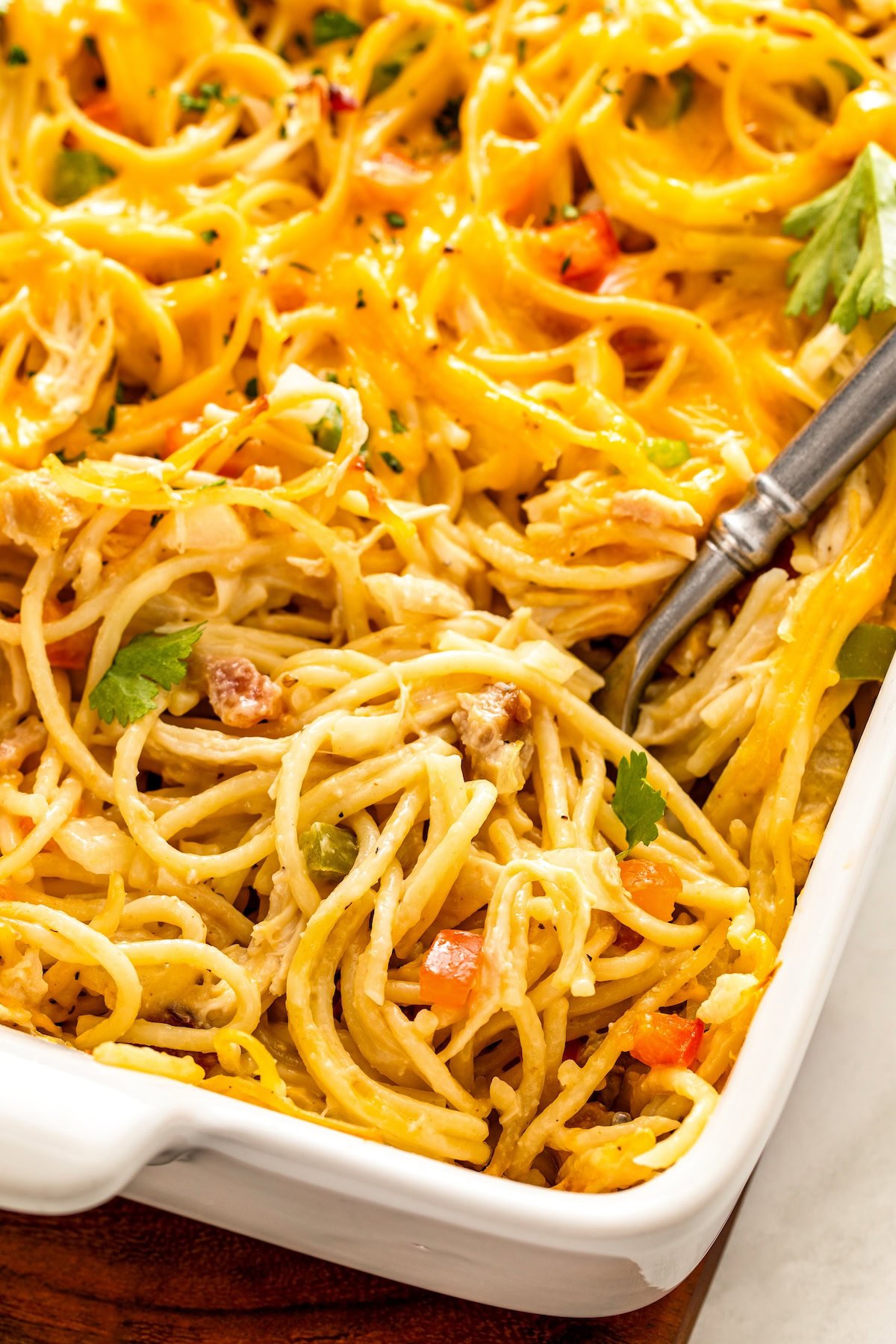 This Chicken Spaghetti recipe is quick, easy, and loaded with flavor. The secret? It's loaded with bacon and a delicious creamy cheese sauce! A large serving spoon is placed in a baking dish filled with cheesy bacon and chicken spaghetti pasta.