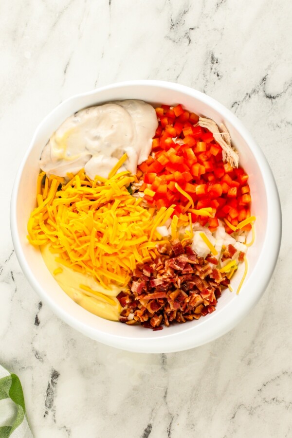 This Chicken Spaghetti recipe is quick, easy, and loaded with flavor. The secret? It's loaded with bacon and a delicious creamy cheese sauce! Creamy soup, chopped vegetables, bacon, cheddar cheese and shredded chicken are placed in a mixing bowl.