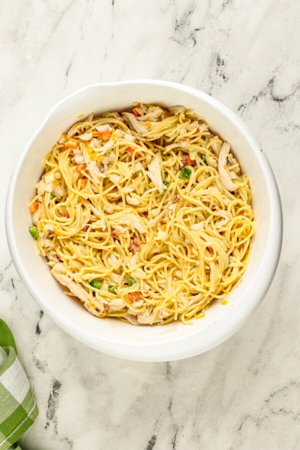 This Chicken Spaghetti recipe is quick, easy, and loaded with flavor. The secret? It's loaded with bacon and a delicious creamy cheese sauce! Cooked spaghetti is mixed in a bowl with chopped vegetables and shredded chicken.