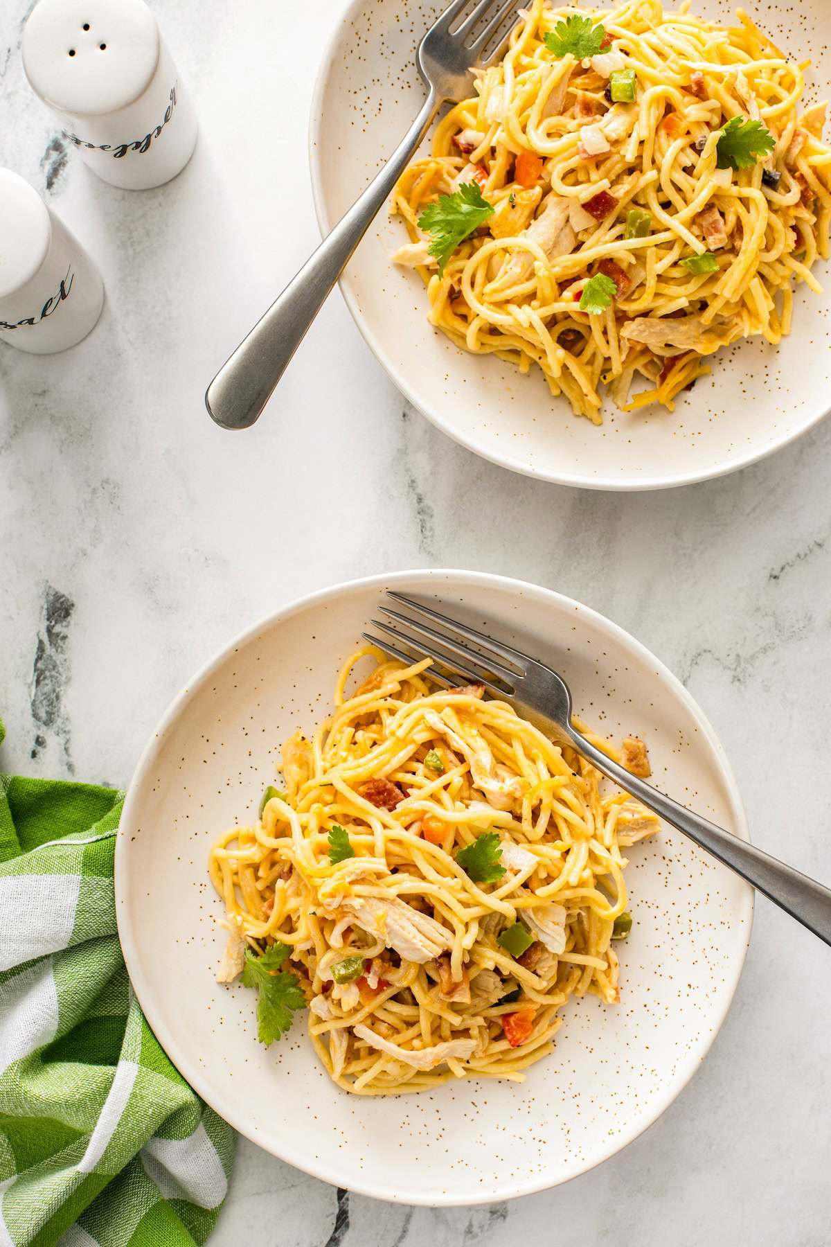 This Chicken Spaghetti recipe is quick, easy, and loaded with flavor. The secret? It's loaded with bacon and a delicious creamy cheese sauce! Two plates are topped with portions of pasta, chicken and vegetables.