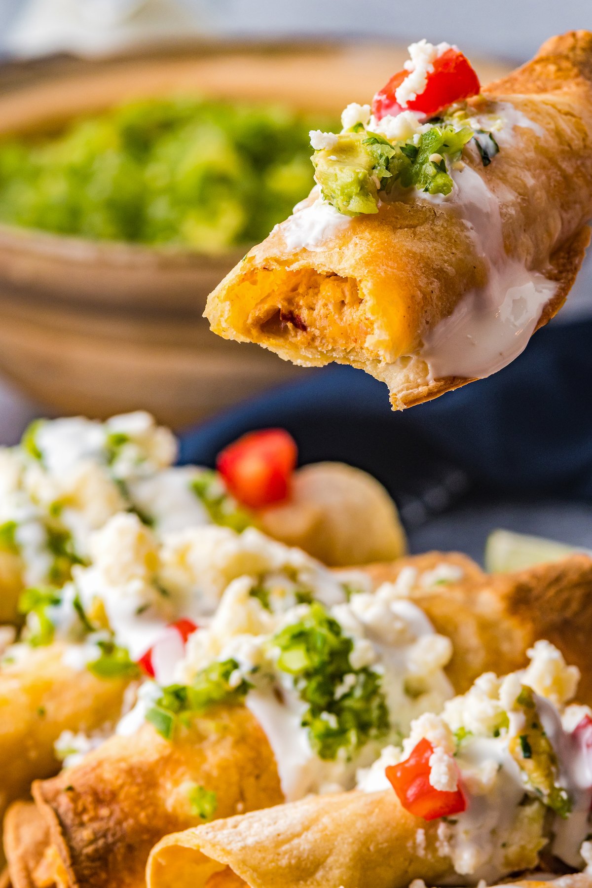 A plate of taquitos. One is held close to the camera, with a bite out of it to show texture.