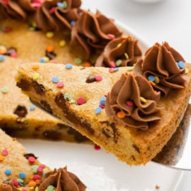 A slice of cookie cake being lifted from a white plate.