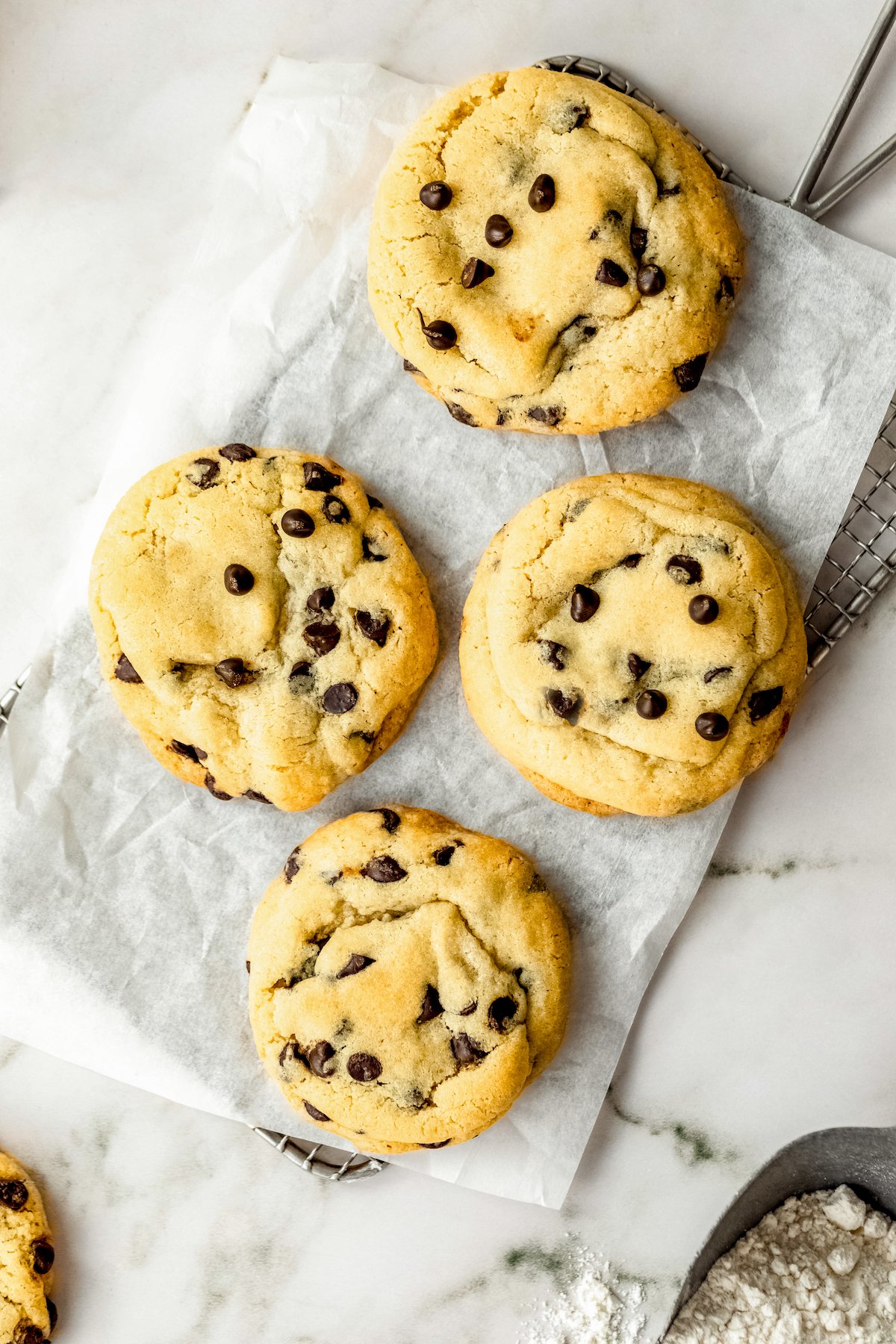 With no chilling required, this easy chocolate chip cookie recipe creates thick cookies with crisp edges and soft, chewy centers in 30 mins! Four large soft chocolate chip cookies with crisp edges and chewy centers arranged on a cooling rack lined with parchment paper after baking.