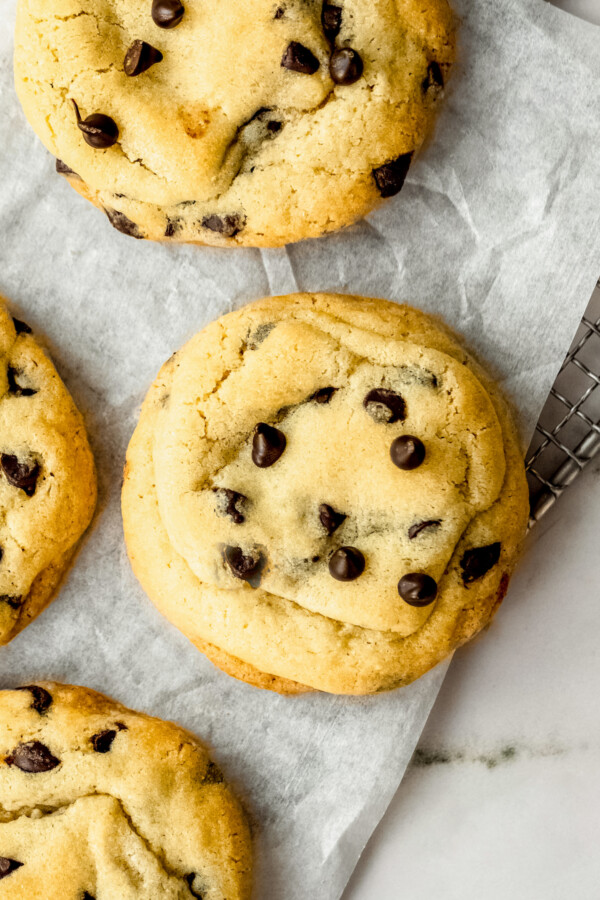 With no chilling required, this easy chocolate chip cookie recipe creates thick cookies with crisp edges and soft, chewy centers in 30 mins! Four freshly baked homemade easy chocolate chip cookies on a cooling rack lined with parchment paper.