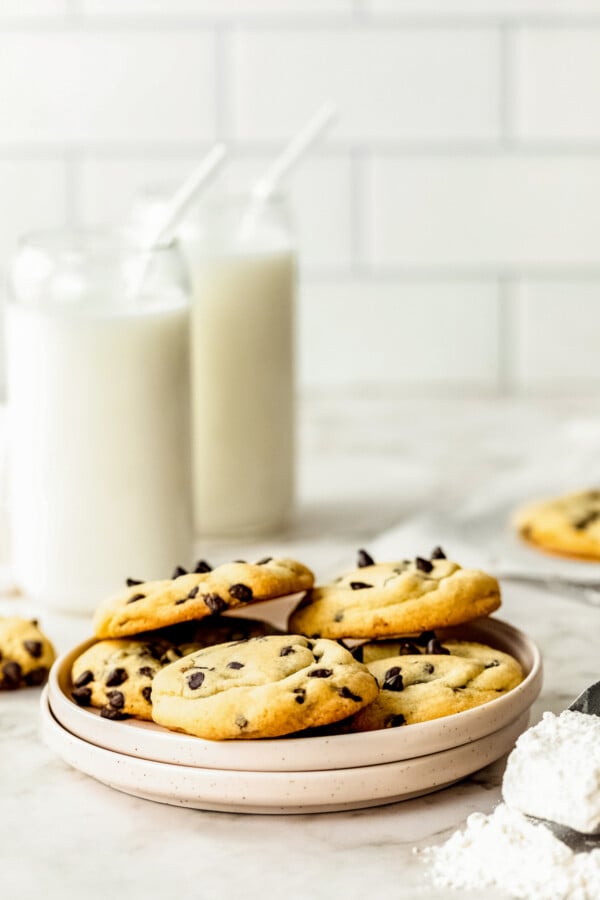 With no chilling required, this easy chocolate chip cookie recipe creates thick cookies with crisp edges and soft, chewy centers in 30 mins! A plate of homemade chocolate chip cookies arranged on a plate with two large glass cups of milk.